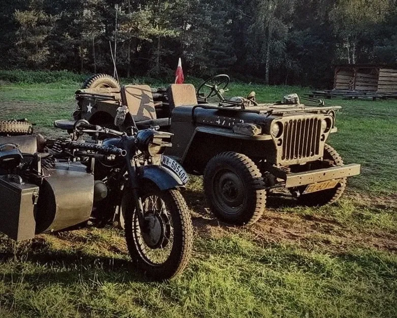 Wojskowy jeep i motocykl z wózkiem bocznym na trawie, w tle las i polska flaga